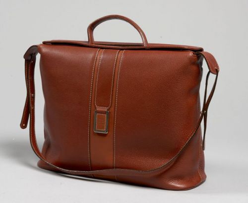 COURREGES, Sac d'épaule en cuir cognac souple parcouru d'une bande en cuir tabac. Une anse bandoulière réglable, une poignée sous rabat. Plaque en métal argentée recouverte de cuir monogrammé. Deux grandes poches plaquées à l'arrière. Double rabat magnéti