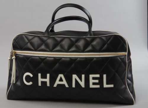 CHANEL, Sac de sport en cuir matelassé noir fermant par zip, parmentures en cuir blanc, le nom de la Maison inscrit en blanc des deux cotés, une poche zippée d'un côté, base en cuir lisse à cinq patins dorés, intérieur en cuir noir à une poche zippée. 26 