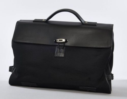 MONTBLANC, Porte document en cuir et coton noir, rabat à une poignée, dos à une poche plaquée et un passant pour poignée de valise à roulette, pates de serrage sur chaque côté, fermeture par boutonnière à élastique et bouton siglé, deux aimants sous le ra