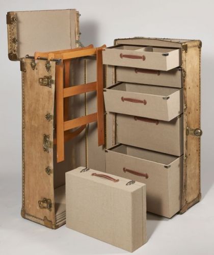 ANONYME, Grande malle-cabine en bois recouverte de vélin, garnitures en laiton, l'intérieur à cinq tiroirs, une mallette et une penderie pouvant former bibliothèque à cinq étagères, entièrement retapissé de toile sable et poignées en cuir naturel surpiqué