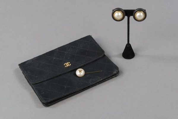 CHANEL POCHETTE à rabat en satin matelassé marine, fermoir pression rehaussé du sigle en métal doré strassé (petite patine d'usage, manque un strass). Nous y joignons une FIBULE perlée siglée (signée) ainsi qu'une PAIRE de CLIPS d'OREILLES en bois et méta