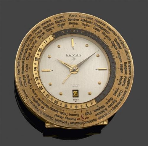 LUXOR. WORLDTIME. Réveil de chevet en laiton doré. Lunette gravée des villes du monde avec second fuseau horaire et indication jour nuit. Cadran argenté avec guichet dateur à 6h. Mouvement mécanique 8 jours. Cadran signé.. Numérotée 1005.. Diam. 76 mm. Ec